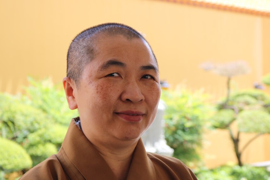 A buddhist nun wearing moddest brown robes and a shaved head gently smiling. 