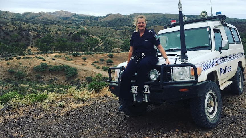 A policewoman sits on a four-wheeled-drive police car with mountains in the background