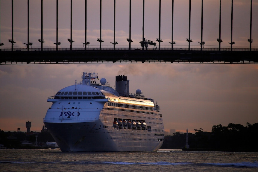 A P&O cruise ship sails under a bridge in sunset 