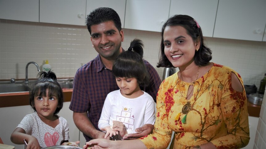 A man and woman and two small girls standing in a kitchen smiling and making Nepalese dumplings