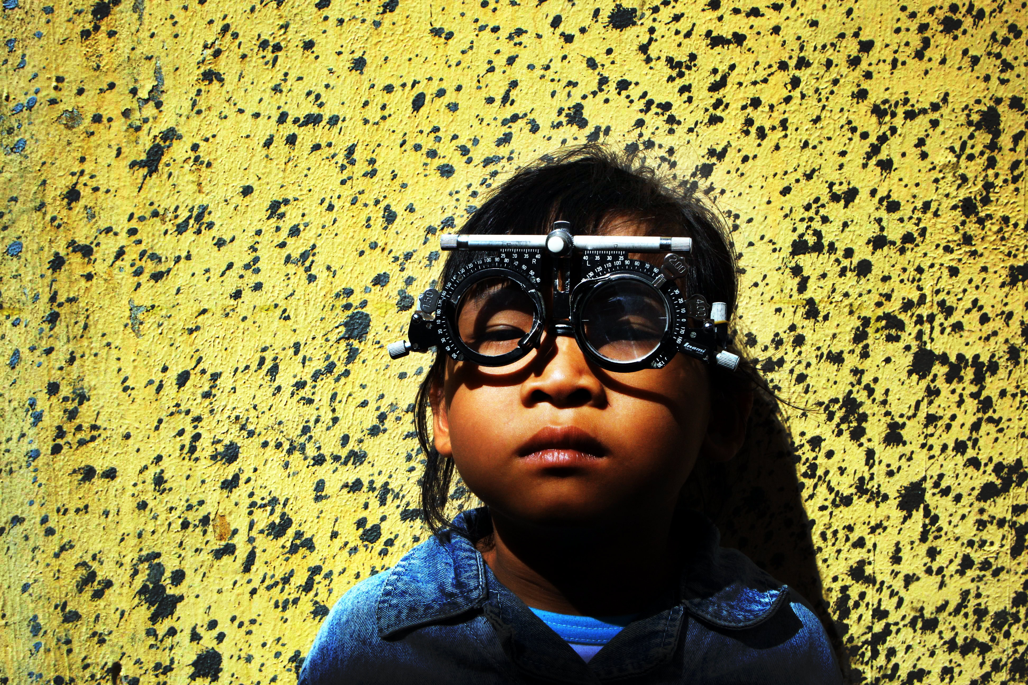 Boy with optometrist glasses on standing against yellow wall.