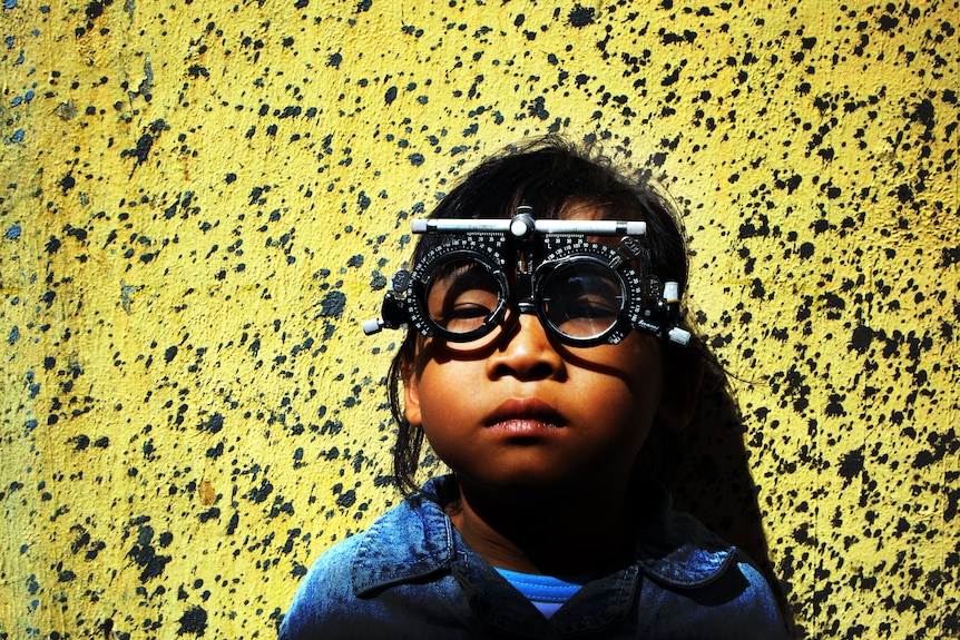 Boy with optometrist glasses on standing against yellow wall.