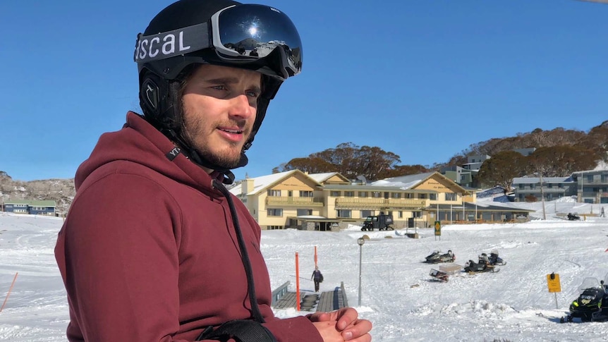 Sam Tait looks into the distance wearing ski equipment including helmet and ski poles.