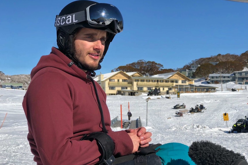 Sam Tait looks into the distance wearing ski equipment including helmet and ski poles.