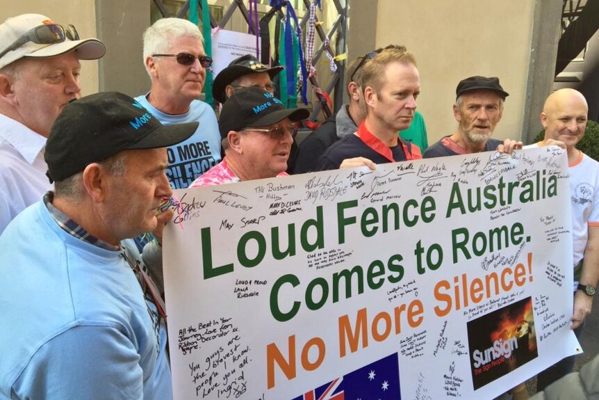 Survivors of clergy abuse hold a Loud Fence sign in front of the gates, with ribbons on it, of the Domus Australia.