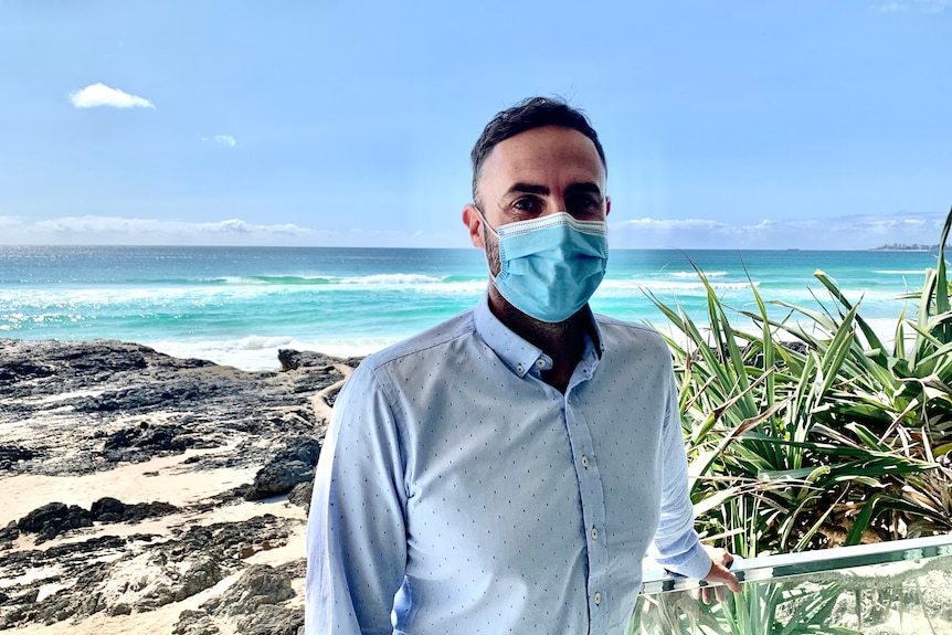 Currumbin Surf Lifesaving Club CEO Michael Sullivan wearing a mask standing on the club balcony overlooking beach