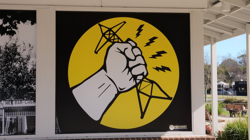 bold yellow and black sign opposing energy transmission towers outside supermarket
