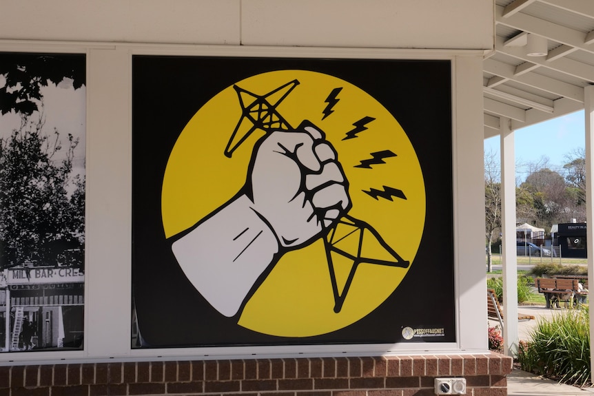 bold yellow and black sign opposing energy transmission towers outside supermarket