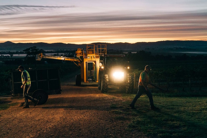 Two people walk in front of a tractor with sunrise in the background.