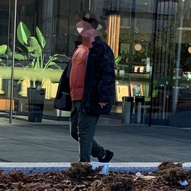 An unidentifiable man walks in front of a cafe.