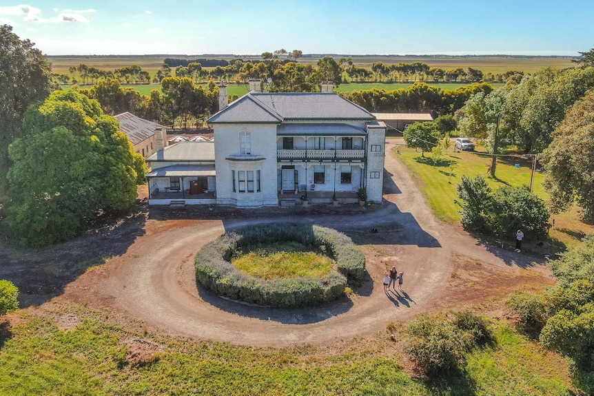 An aerial photo of an old two-storey white stone mansion surrounded by a large ring of lavender and green lush trees and lawn.