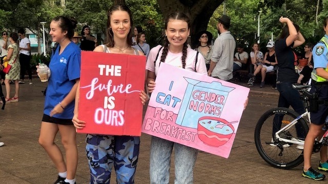 Two teenagers hold signs saying"The future is our" and "I eat gender norms for breakfast".