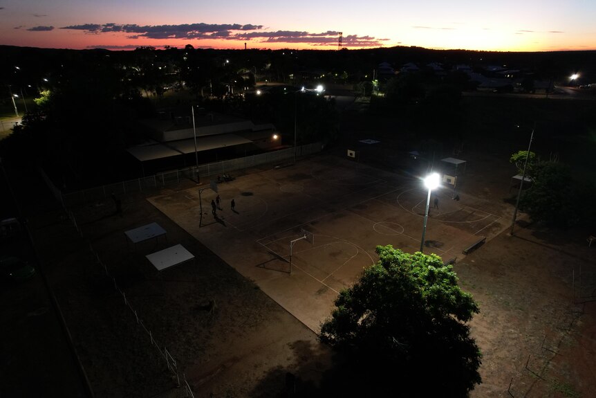 Children play basketball on a court at dusk