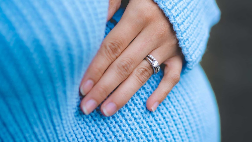 in the picture you can see a pregnant woman's torso, she's wearing a turquoise blue jumper and resting a hand on her belly