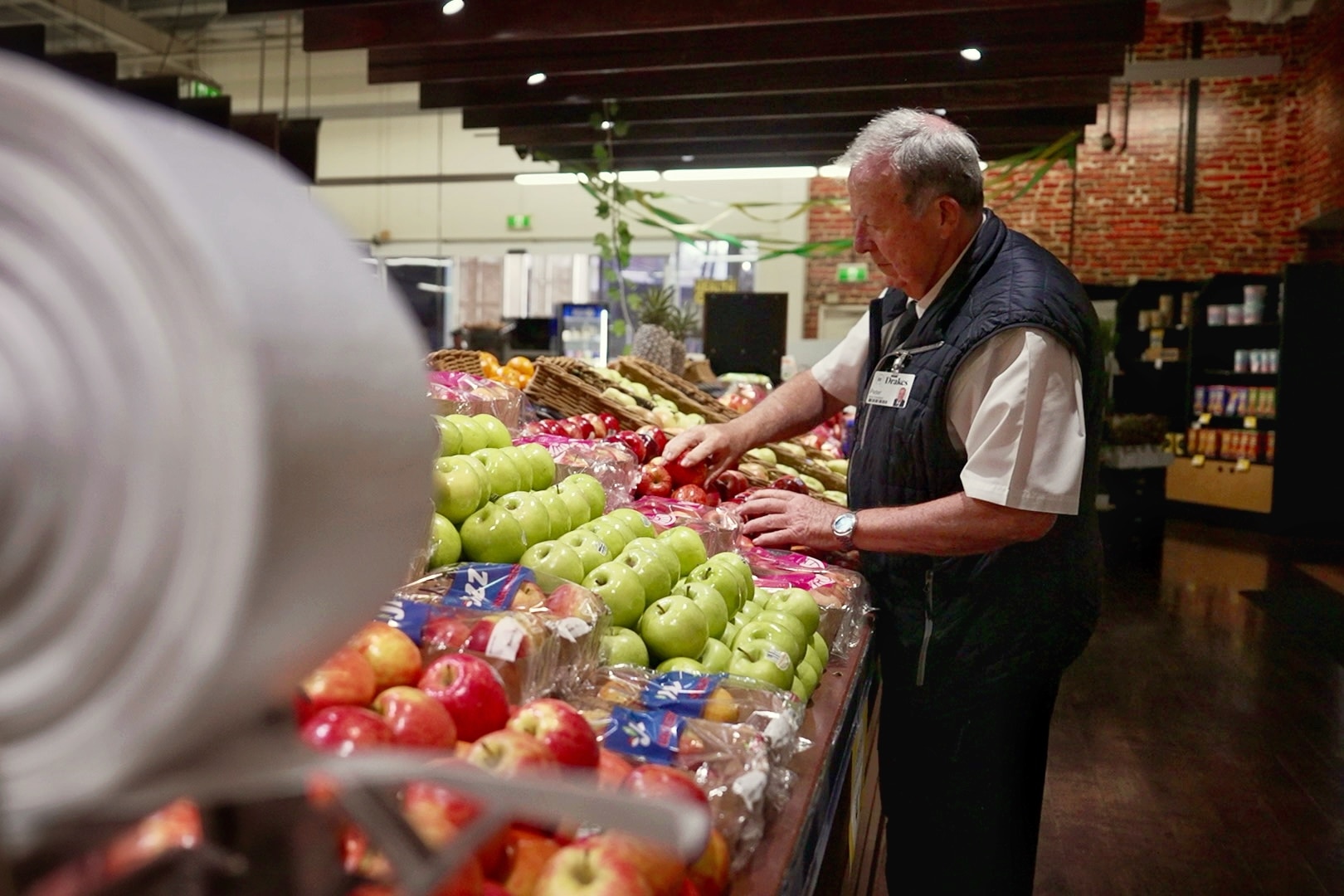 an older man in a supermarket uniform looks at the fruit