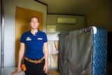 A woman standing in a dark hotel room with an overturned bed