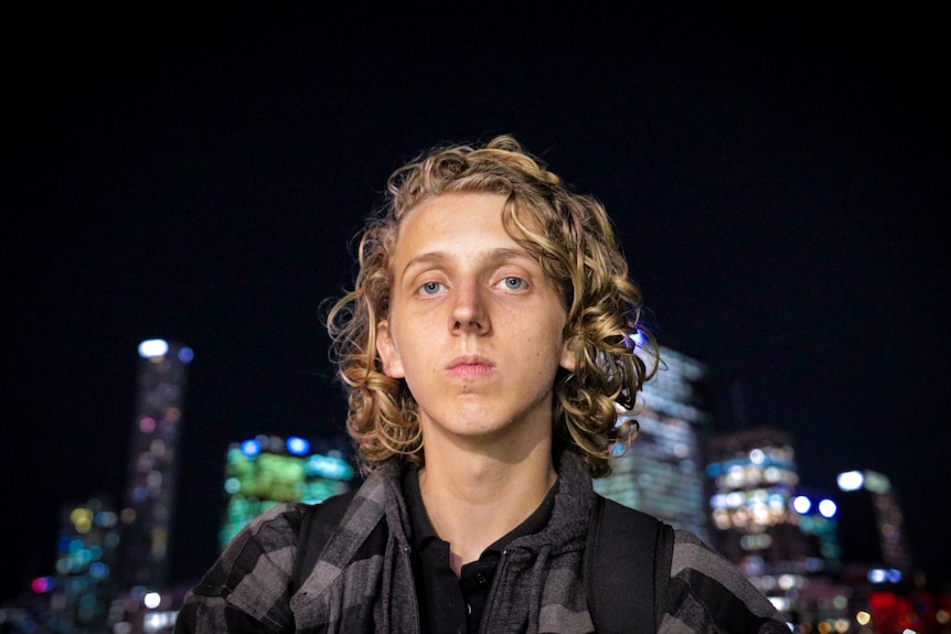 young person with curly blonde hair with nighttime cityscape behind them