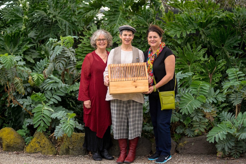 Three women hold a replica Wardian case in front of plants