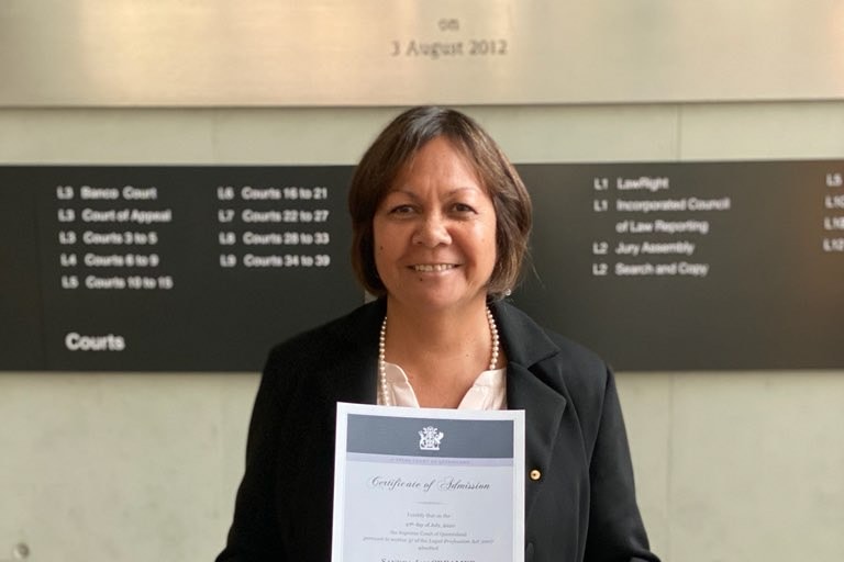 A woman in business clothes smiles holding a certificate of admission