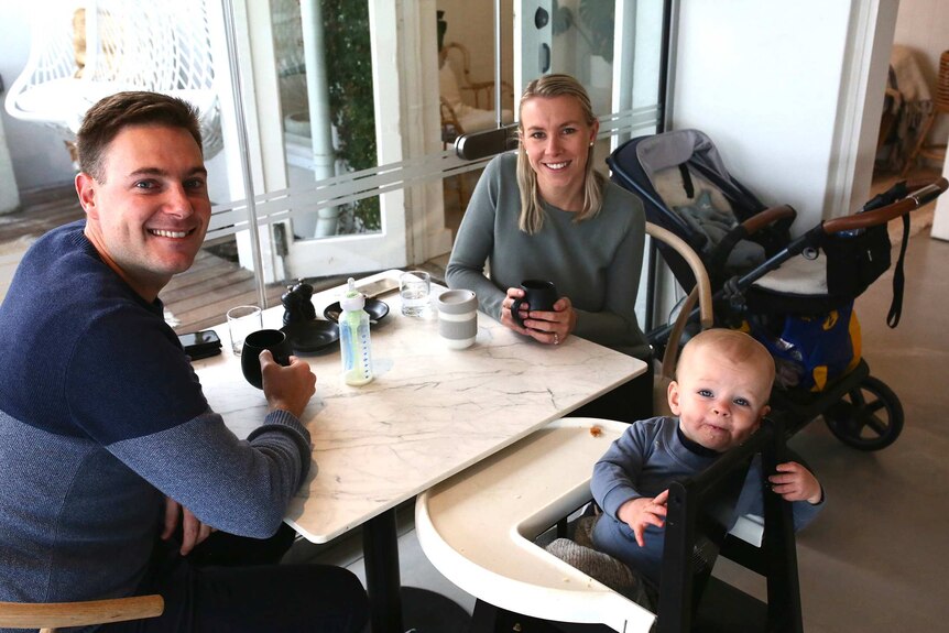 A couple sit at a table in a cafe drinking coffee next to a baby boy.