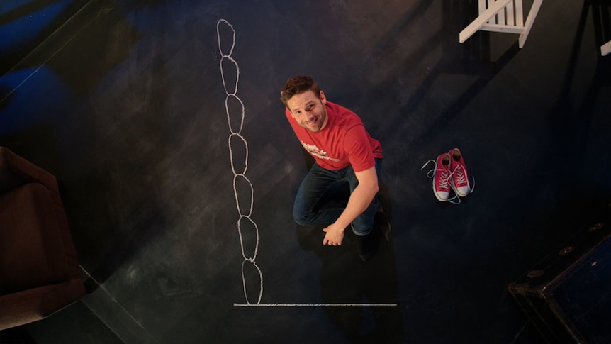 Man sits on floor beside tracings of feet stacked one on top of the other