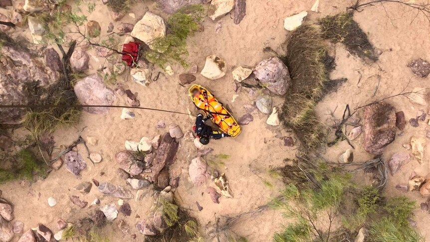 A tourist is strapped into a stretcher to be winched into a helicopter as seen from above.
