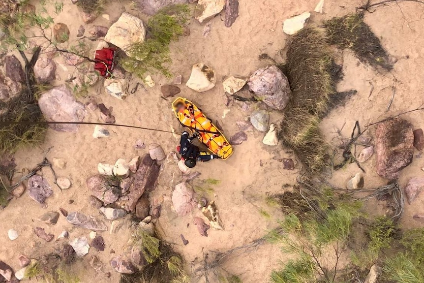 A tourist is strapped into a stretcher to be winched into a helicopter as seen from above.