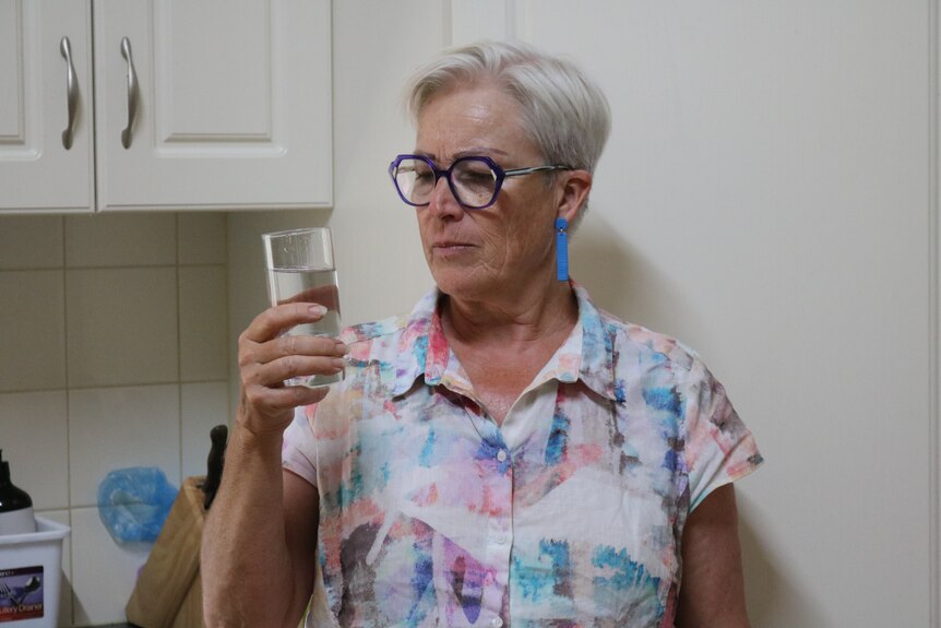 Woman holding and looking at a glass of water in a kitchen.