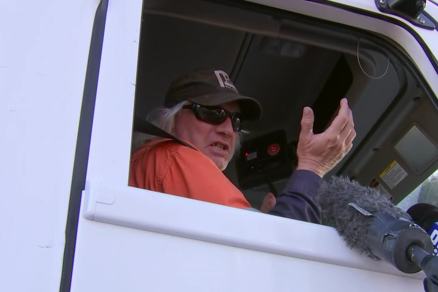 A truck driver gestures from the cabin.