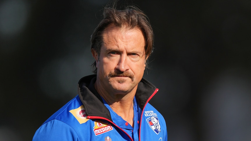 Bulldogs coach Luke Beveridge is pictured walking in his team's blue shirt. The background is obscured and out of focus