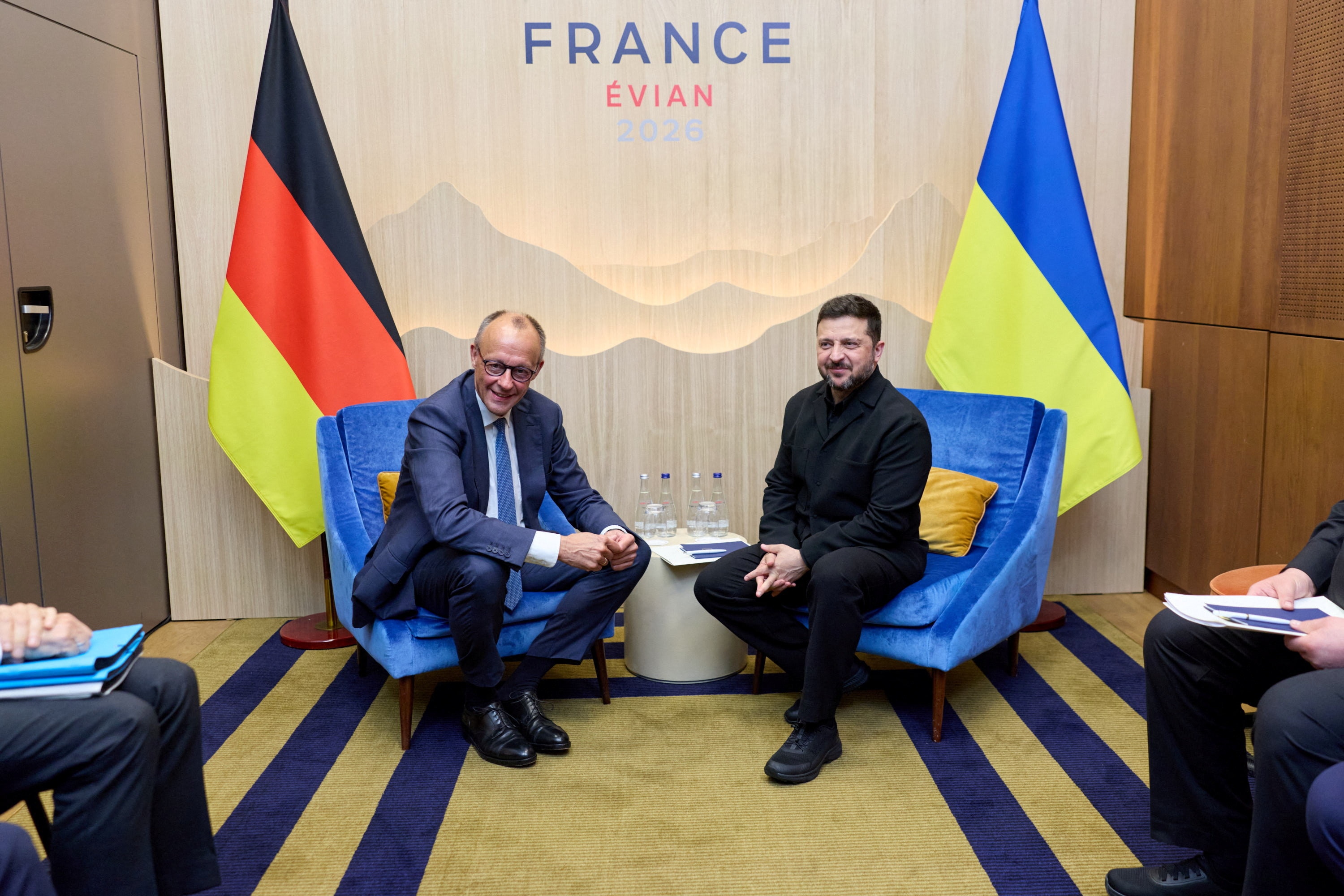 Friedrich Merz and Volodymyr Zelenskyy seated in front of the German and Ukrainian flags.