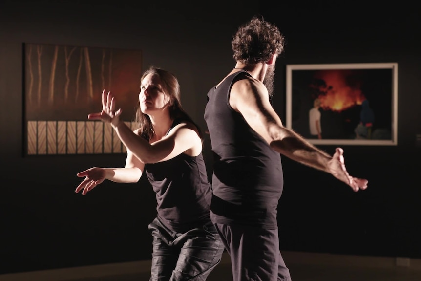 A woman and a man in a dimly lit room perform a choreographed dance