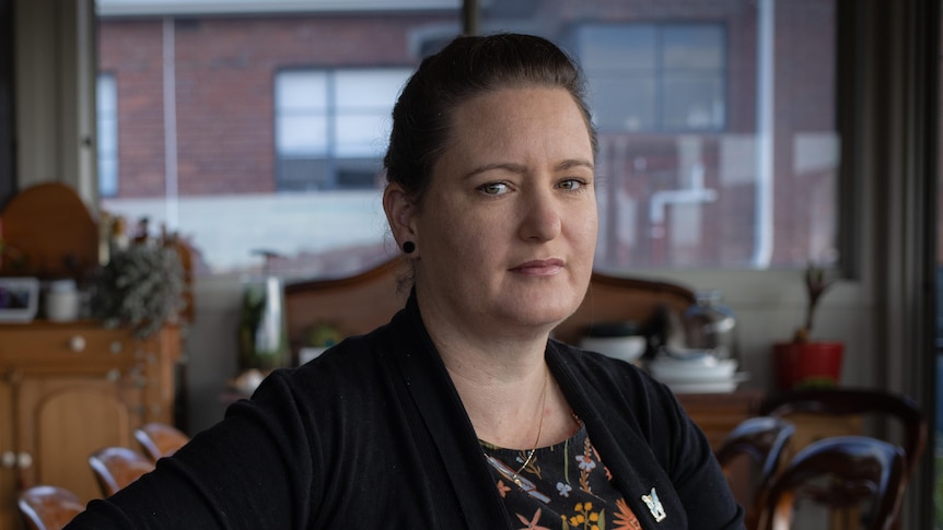 Woman with hair tied back looks directly into the camera, not smiling.