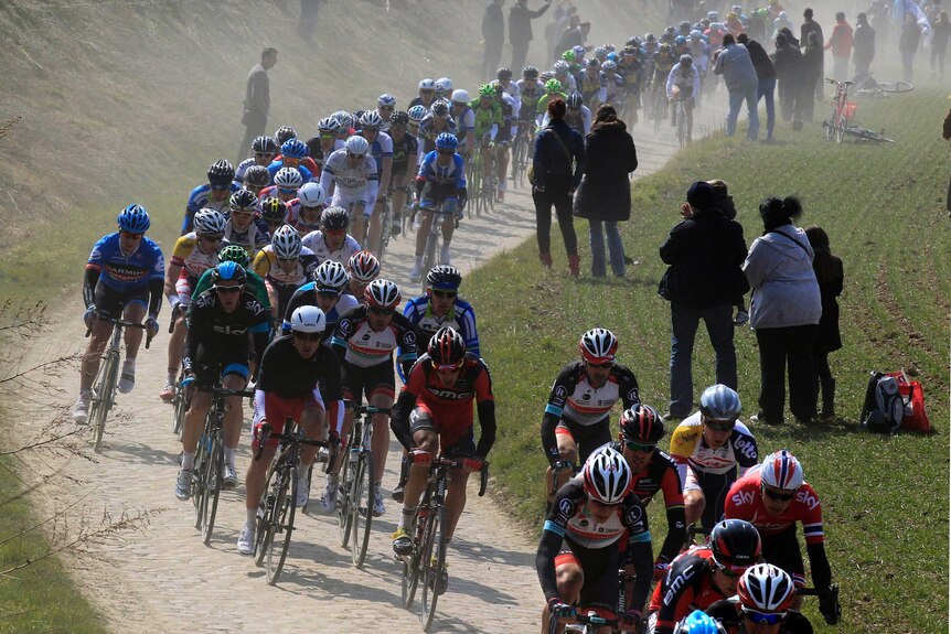 Dust rises as professional cyclists clatter along the cobblestones in a section of Paris-Roubaix.
