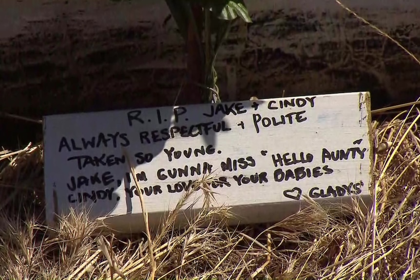 A piece of wood with writing on it pays tribute to people killed in a crash