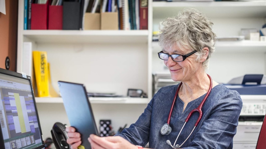 Cohealth GP Heather Dowd sits at her desk and smiles while speaking to a patient via a tablet. She wears a stethoscope.