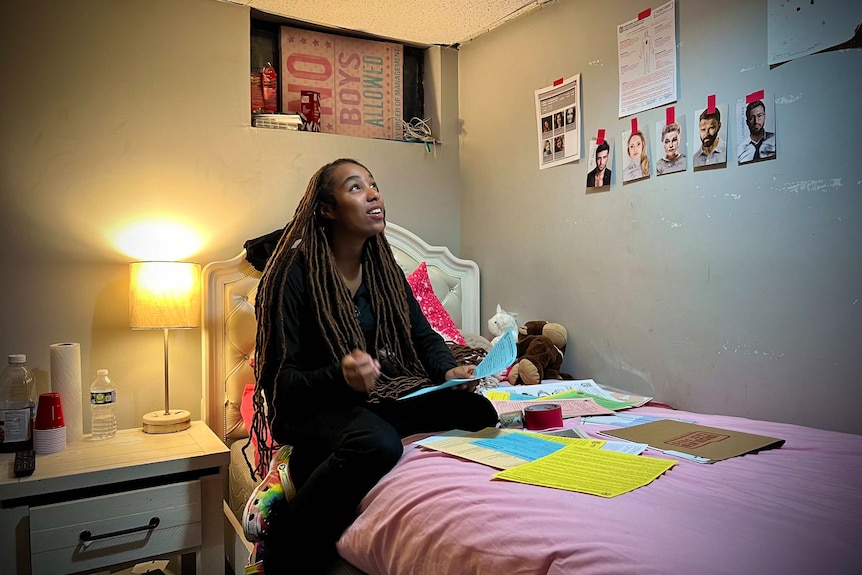 Sakina in her bedroom sits on her bed playing games with papers all around her