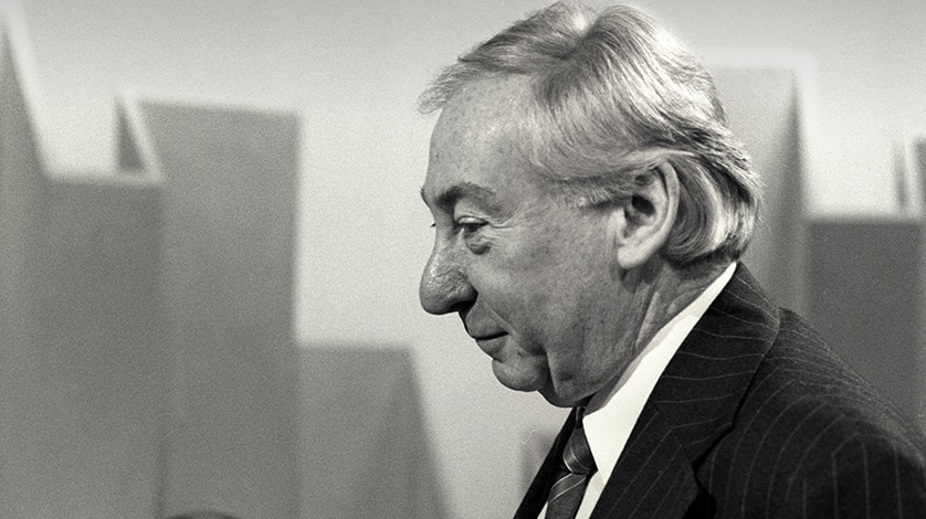 Older man wearing suit grins facing away from camera.