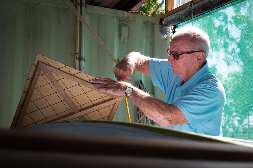 Man in a light blue polo shirt with black sunglasses attaching a part to a wooden boat.