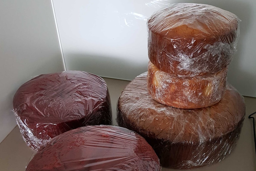 Five cakes of various sizes wrapped in cling wrap, the base of a wedding cake.