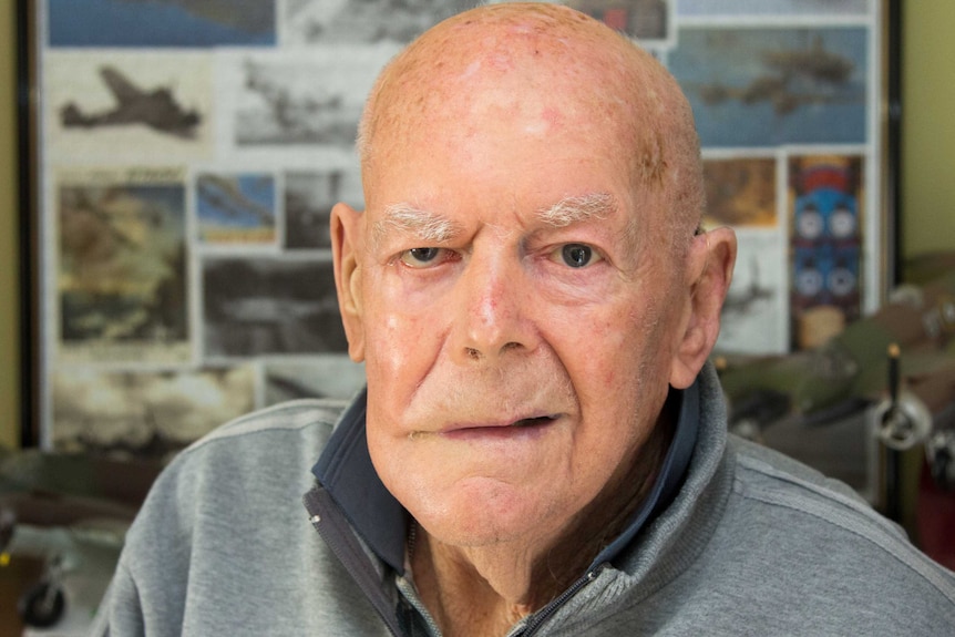 An elderly man looks at the camera, air force memorabilia in background.