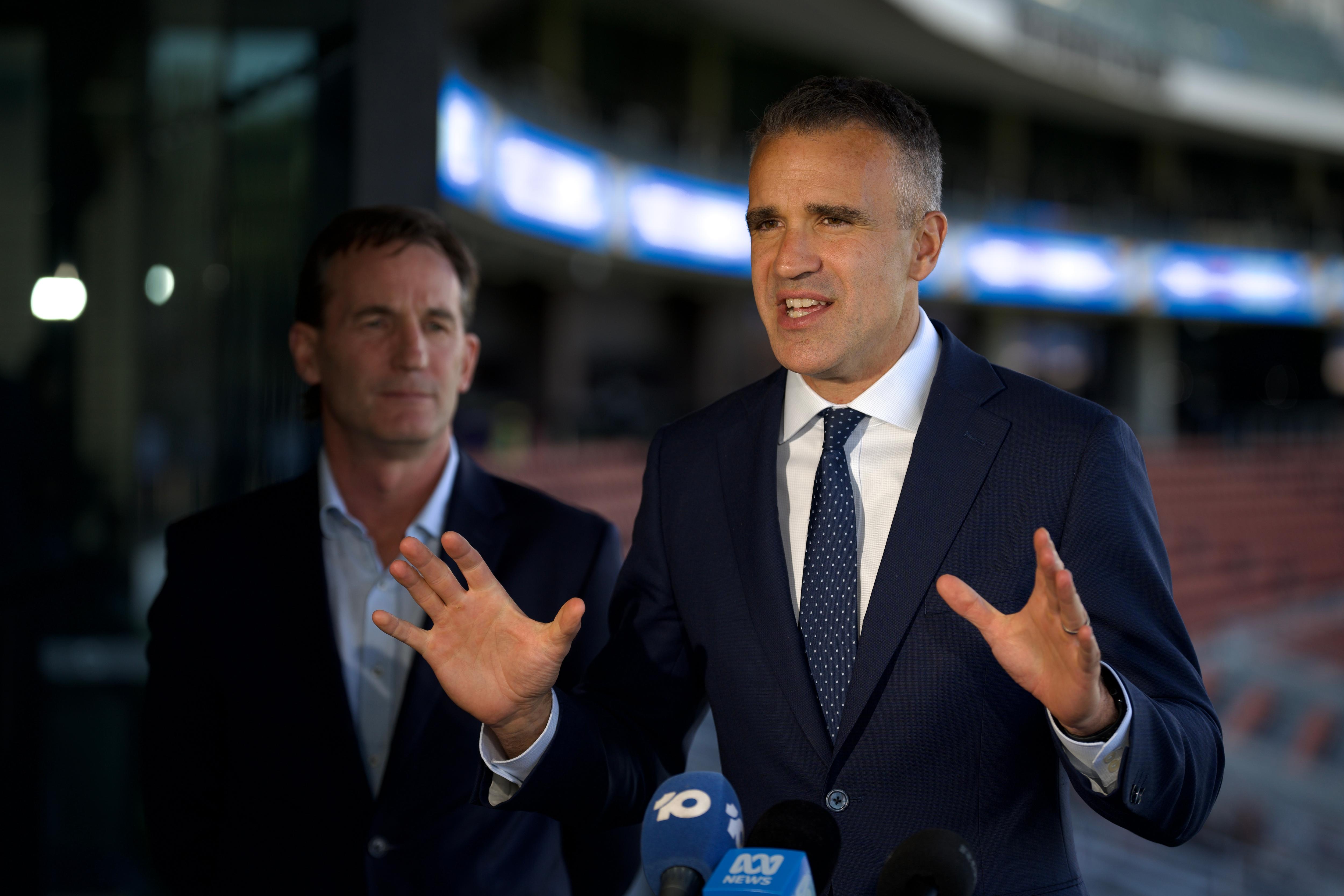 Peter Malinauskas gesturing with his hands while standing next to Andrew Dillon in empty footy stands
