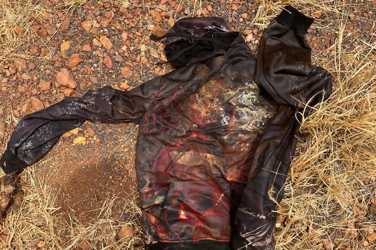 Dirty black jumper lying on red dirt and gravel.