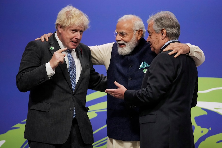 Three men embrace and talk in front of blue screen