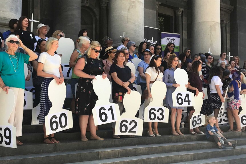 A group of women hold cut-outs labelled with numbers from 1 to 69, representing women murdered across Australia last year.