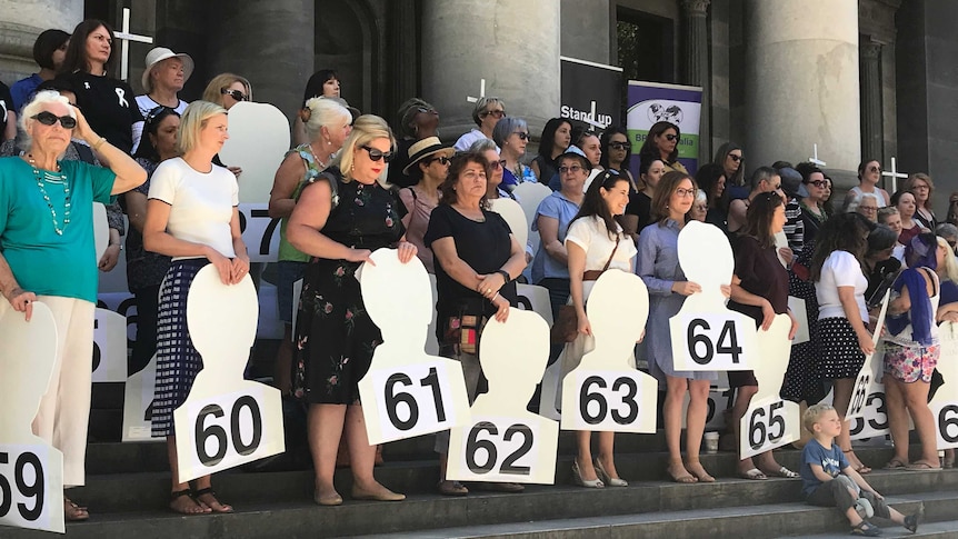 A group of women hold cut-outs labelled with numbers from 1 to 69, representing women murdered across Australia last year.