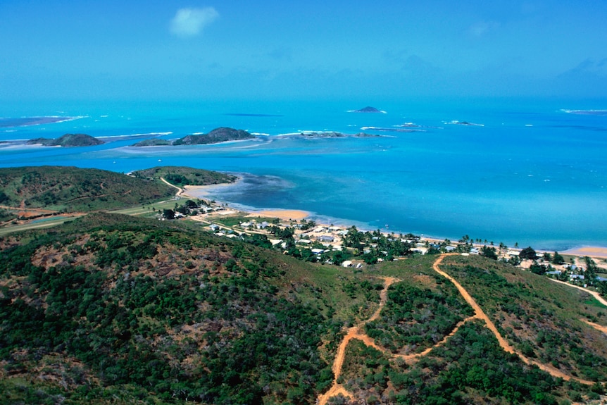 A birds-eye image from a green hill down to crystal blue waters that stretch out to islands in the distance.