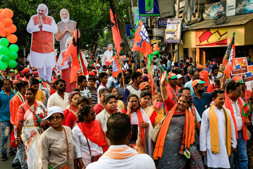 A group of people holding flags and wearing colourful clothes stand in a crowd 