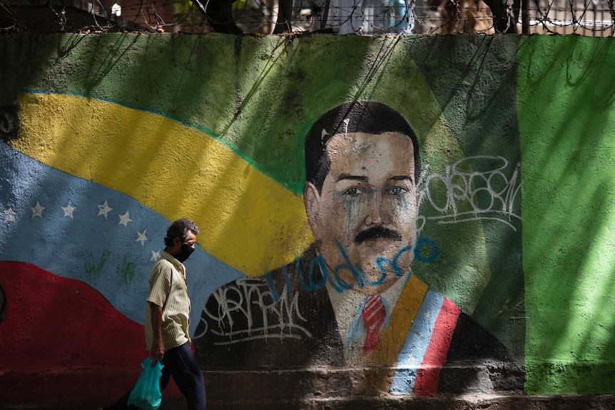 A man wearing a face mask walks past a mural of Venezuelan President Nicolas Maduro