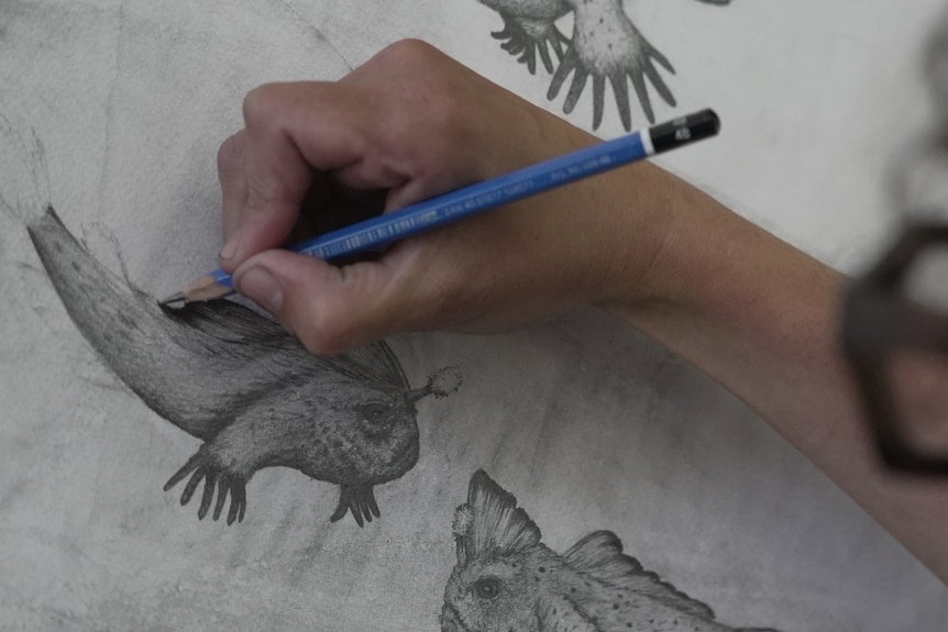 a close up photo of a hand drawing a picture of a handfish with a blue pencil